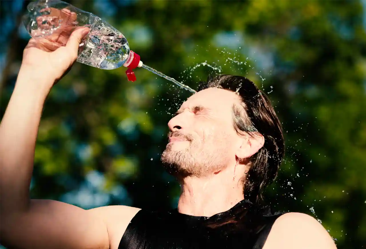 Mann kühlt sich an einem heißen Sommertag mit Wasser aus einer Trinkflasche ab und sorgt bei hohen Temperaturen für Erfrischung.