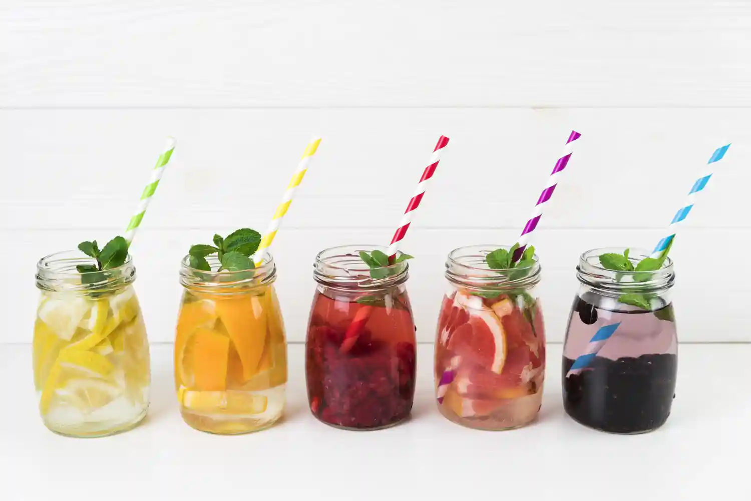 F&uuml;nf Gl&auml;ser mit aromatisiertem Wasser aus Fr&uuml;chten, Beeren und Minze stehen als erfrischende Getr&auml;nke f&uuml;r hei&szlig;e Sommertage bereit.